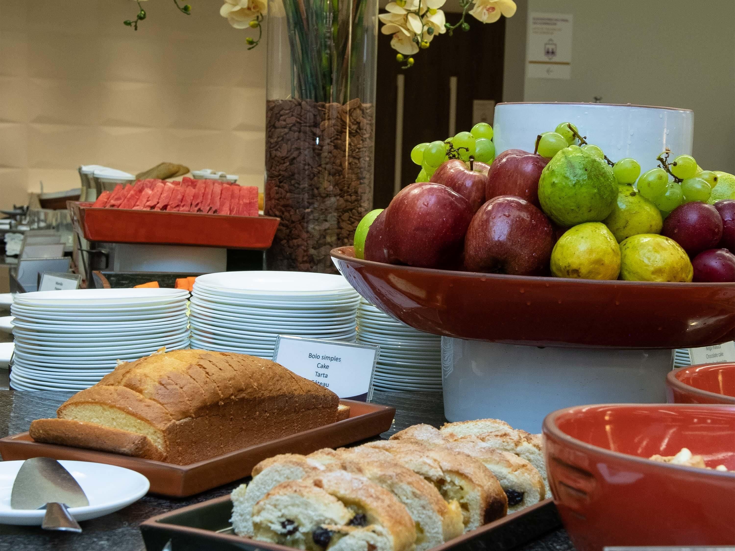 Un bufé con una variedad de alimentos, incluyendo pan, pasteles y un bol de frutas.