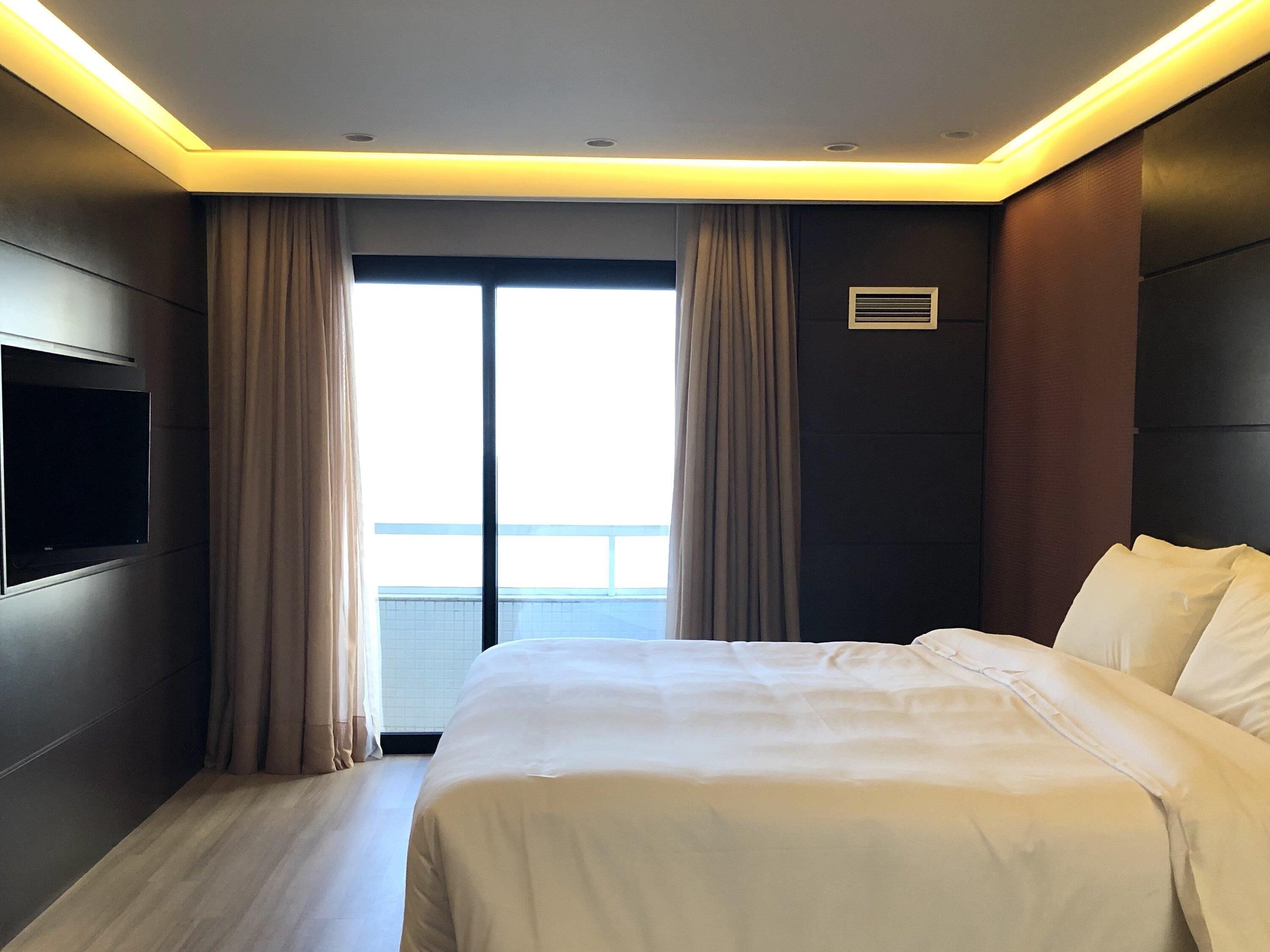 A hotel room with a large bed, a flat-screen TV, and a view of the outside.