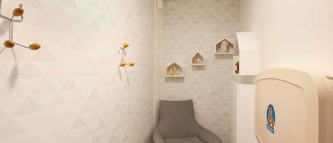 Habitación de esquina con una silla gris, papel tapiz de diseño geométrico, una lámpara de pared y un estante pequeño con adornos.