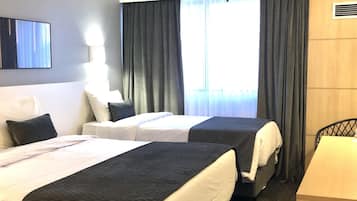 A hotel room with two beds, a desk, a chair, a TV, and a window with curtains.
