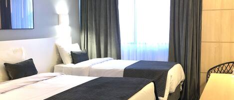 Habitación de hotel con dos camas, un escritorio, una silla, un televisor y una ventana con cortinas.