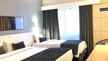 A hotel room with two beds, a desk, a TV, and a window with curtains.