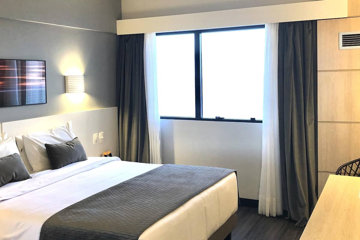 Une chambre dâhĂŽtel avec un lit, une table de chevet, une lampe et une fenĂȘtre avec des rideaux.