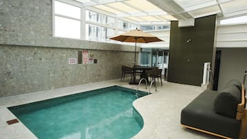Ein Innenpool mit Glasdecke, einem Tisch mit Stühlen und einer Couch.
