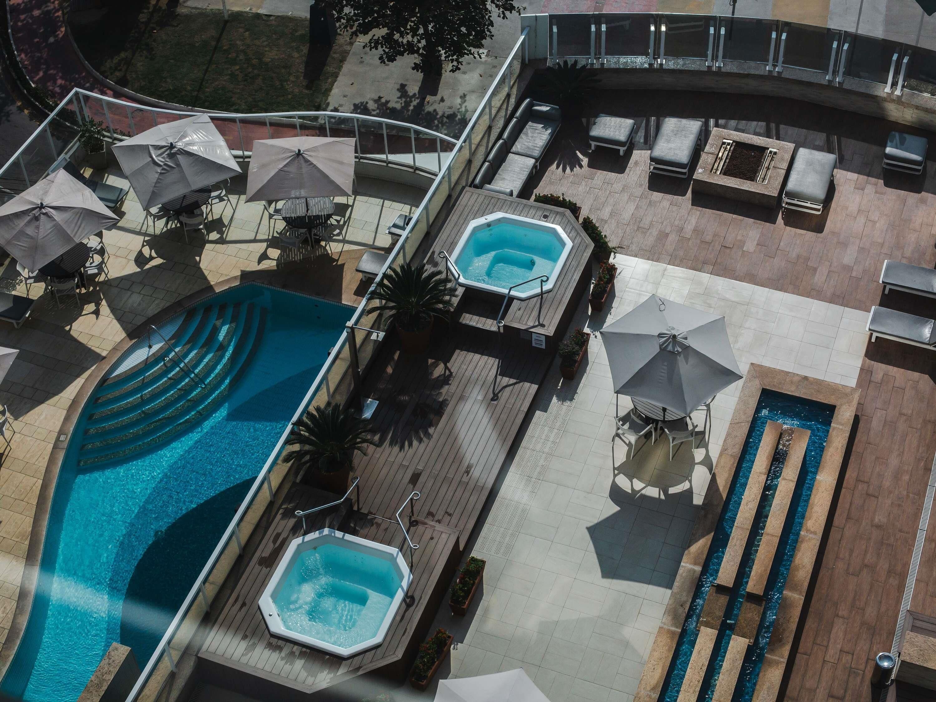 Un espace piscine sur le toit, doté de plusieurs jacuzzis, de chaises longues et de parasols.
