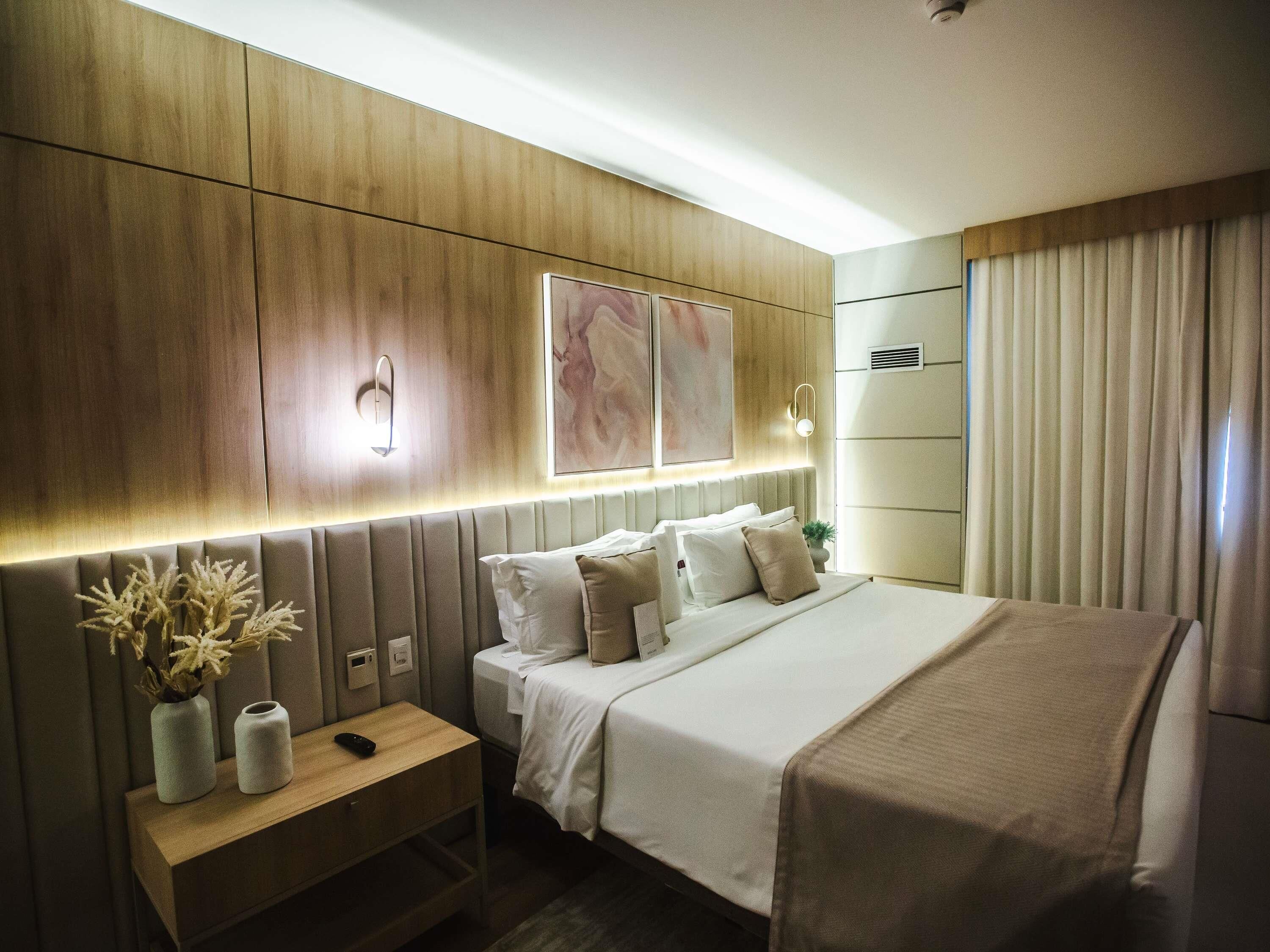 A modern hotel room with a bed, bedside table, wall-mounted light, and artwork.