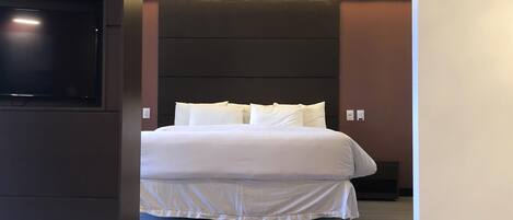 Una habitación de hotel moderna con una cama grande, un televisor de pantalla plana en la pared y una mesita de noche.