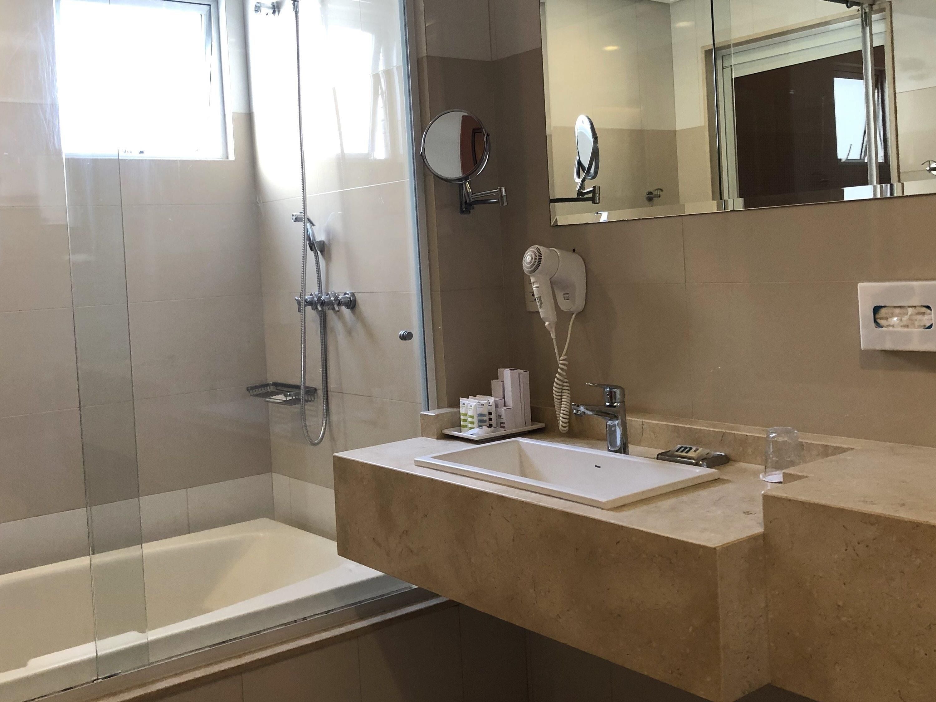 Ein Badezimmer mit Duschkabine aus Glas, einem Waschbecken, einem Spiegel und einem Föhn.