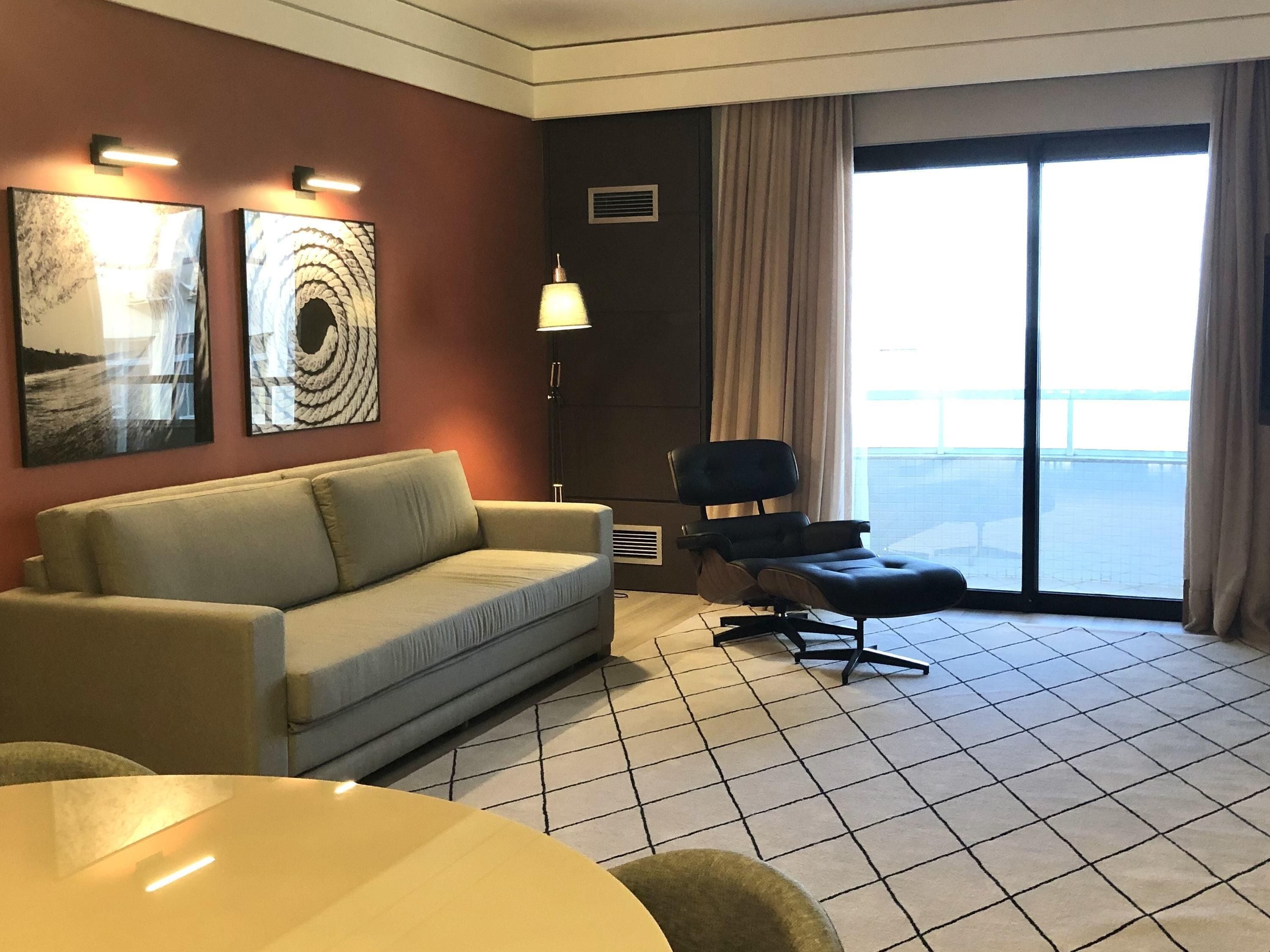 Habitación de hotel con sofá, una silla, una lámpara y vistas al exterior.