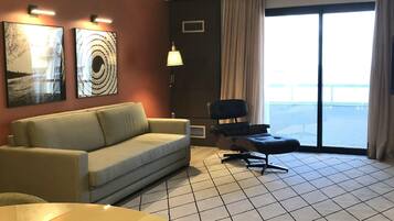 Habitación de hotel con sofá, una silla, una lámpara y vistas al exterior.