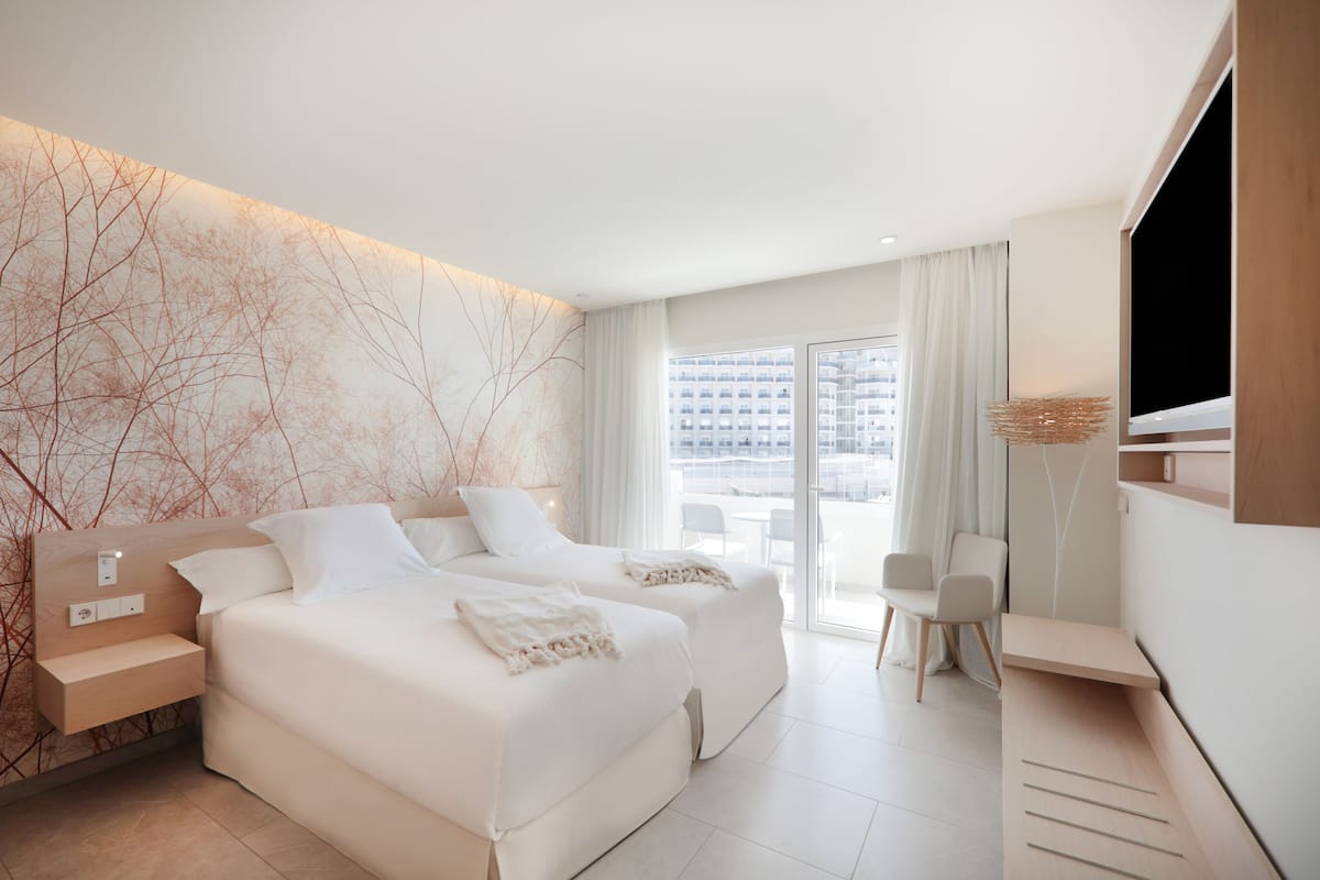 A modern hotel room with two beds, a desk, and a TV.