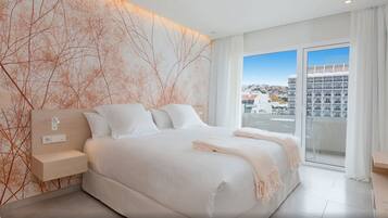 Un dormitorio moderno con una cama grande, una mesita de noche y vistas de la ciudad desde un balcón.