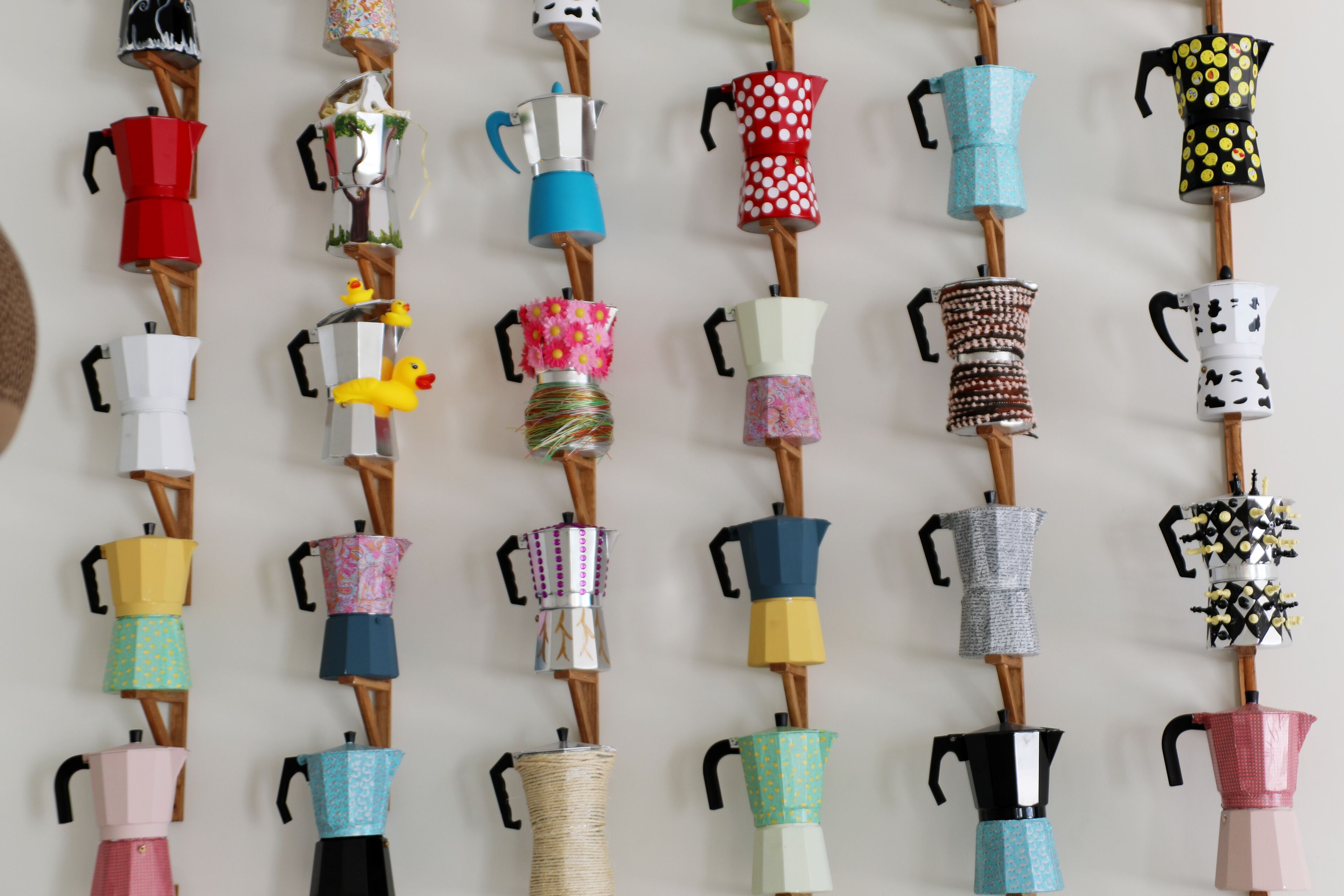 A wall displaying variously designed coffee pots and kettles on wooden stands.