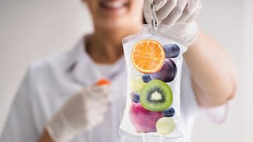 Iemand houdt een doorzichtige plastic zak vol met verschillende soorten fruit.