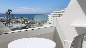 Un balcón con una mesa y una silla blancos, con vistas a una playa y una zona turística.