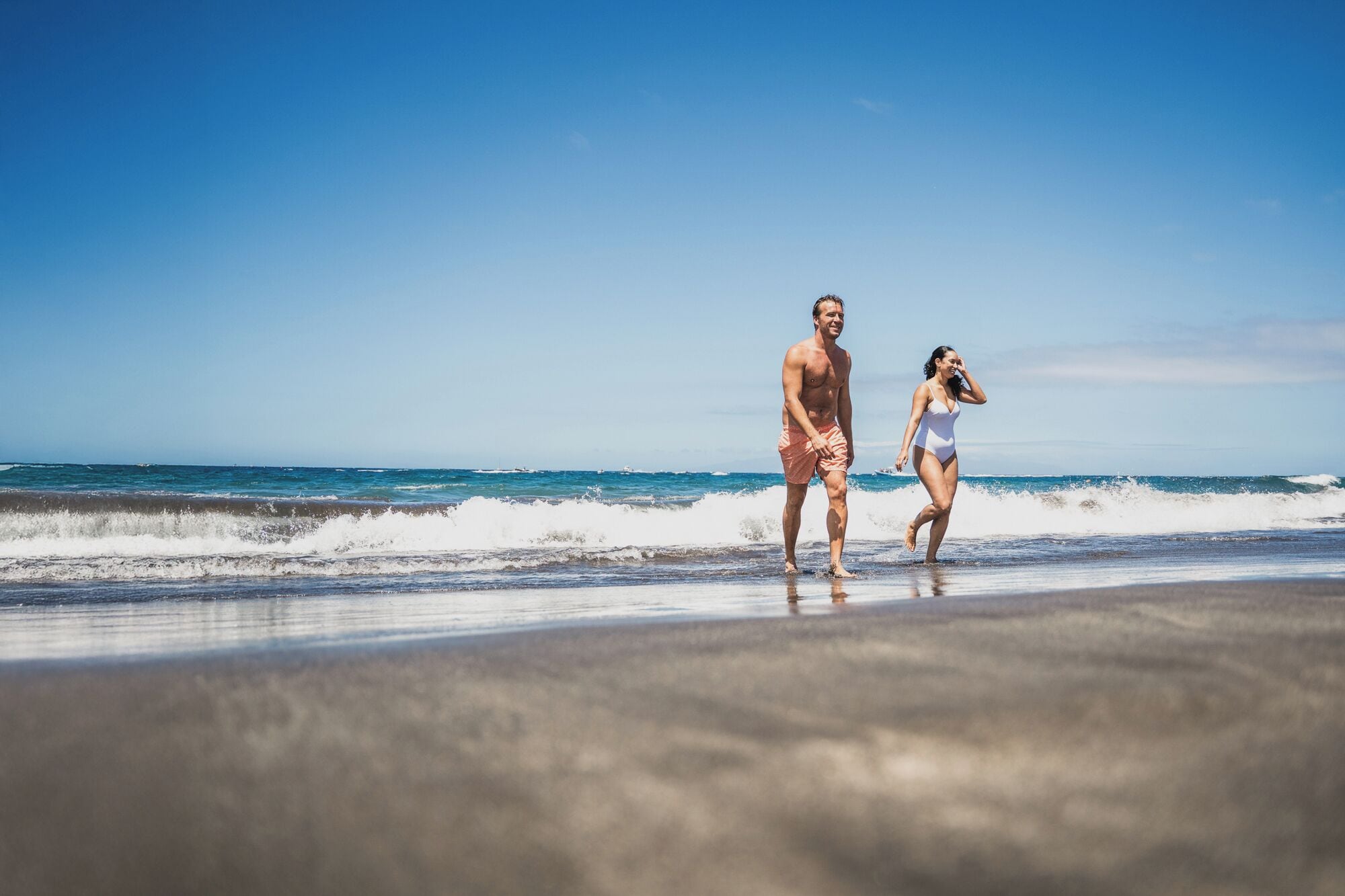 Una playa con dos personas caminando.
