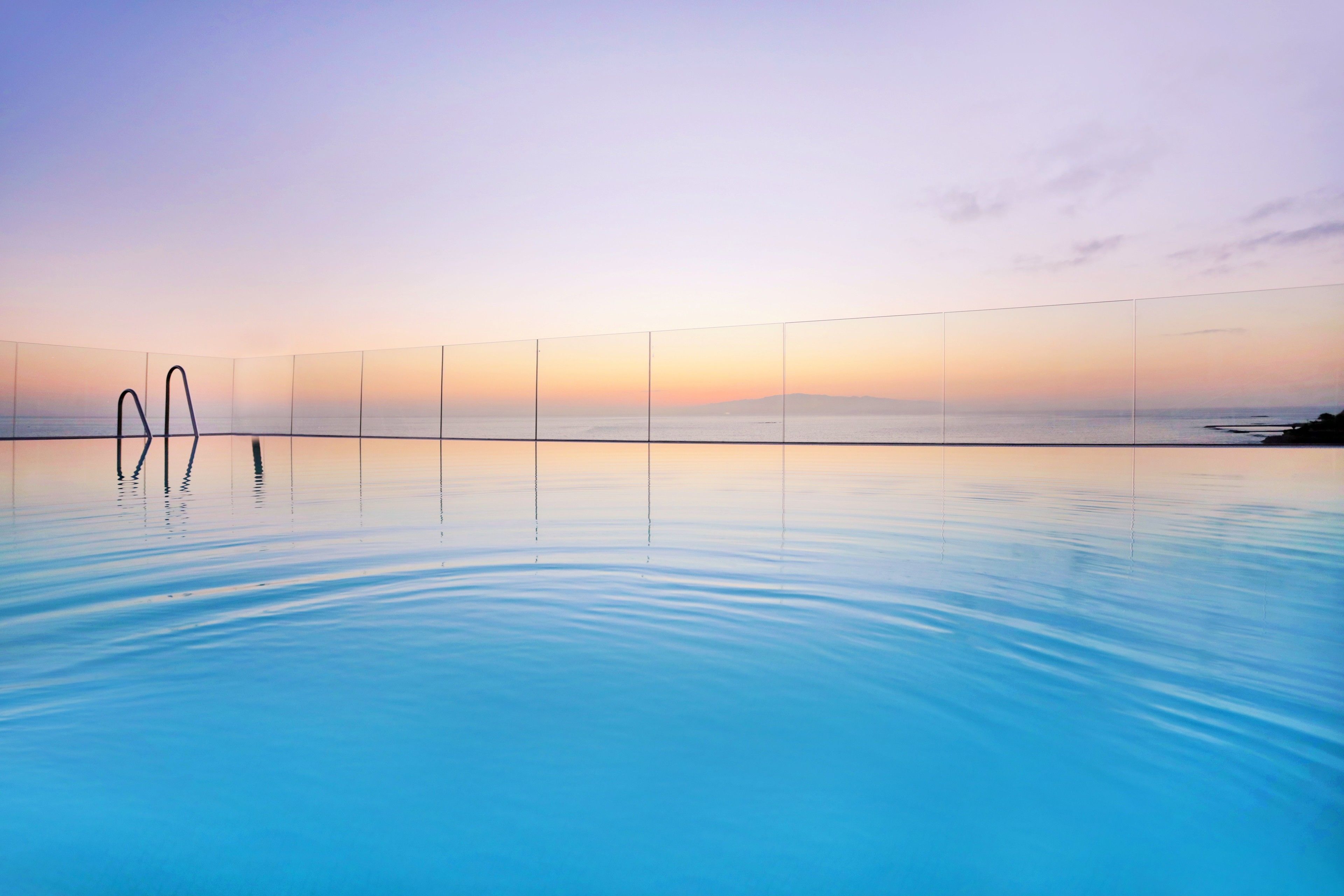 A serene swimming pool with a sunset view, calm water, and a clear sky.