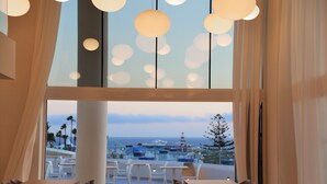 A modern dining area with large windows overlooking a scenic view, featuring a table and chairs arrangement. - Iberostar Selection Sábila - Adults Only (Adeje)