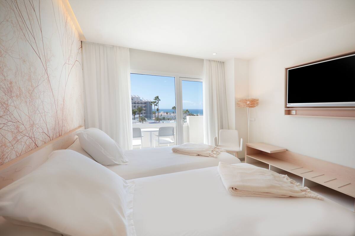 A hotel room with two beds, a TV, a balcony with a view, and a desk.