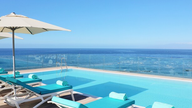 A poolside area with lounge chairs and an umbrella, overlooking a clear blue sea. - Iberostar Selection Sábila - Adults Only (Adeje)