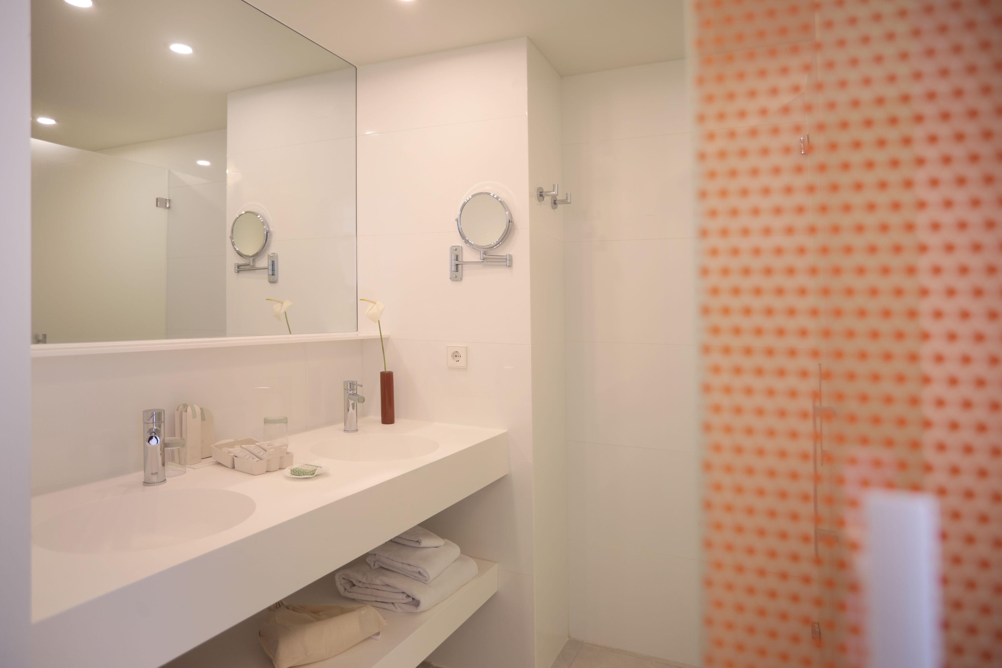 Un baño moderno con tocador blanco, dos espejos, cabina de ducha de vidrio y un perchero para toallas.