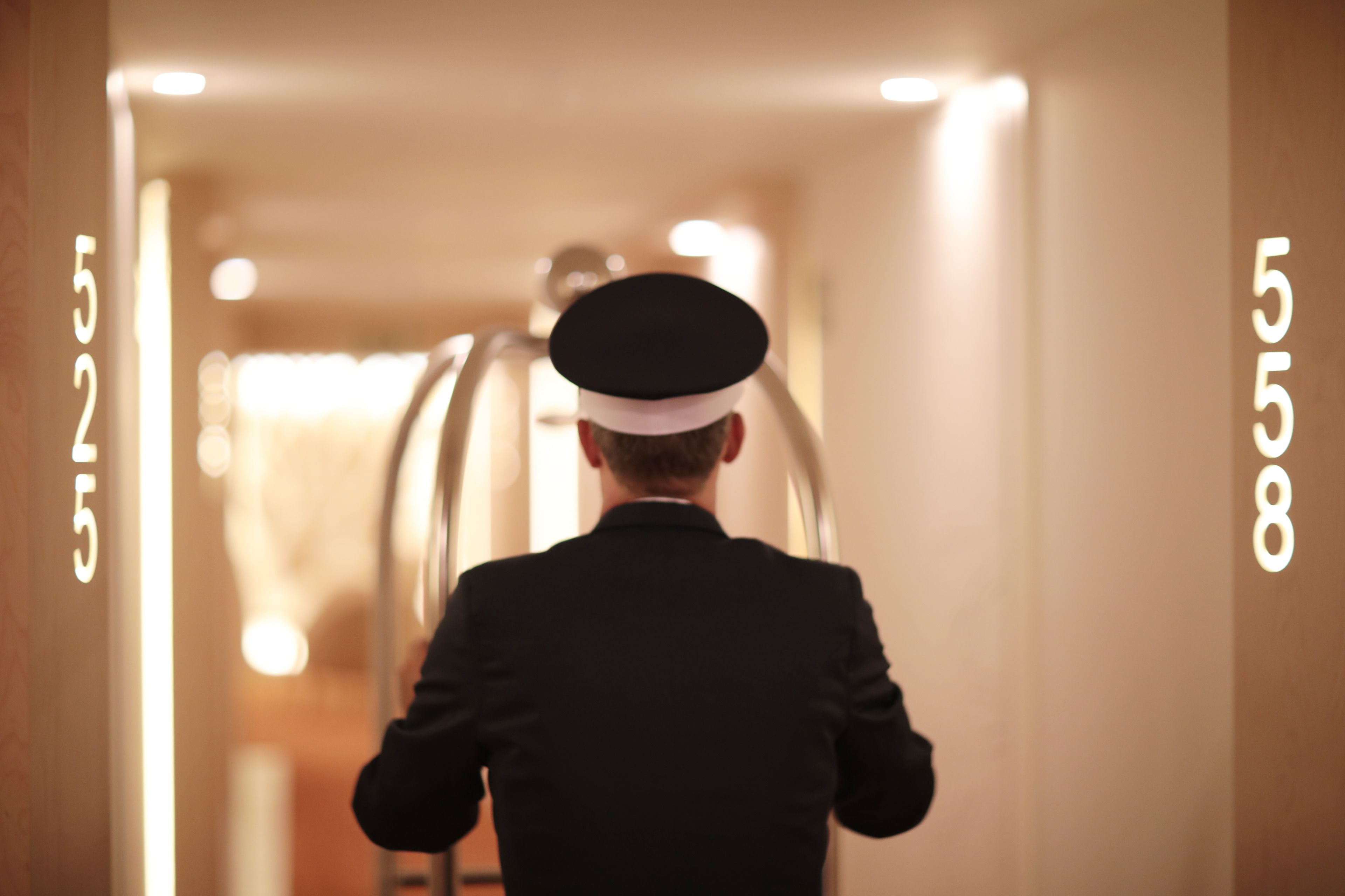 A man in a black suit and white cap walking down a hallway with illuminated numbers on the walls.