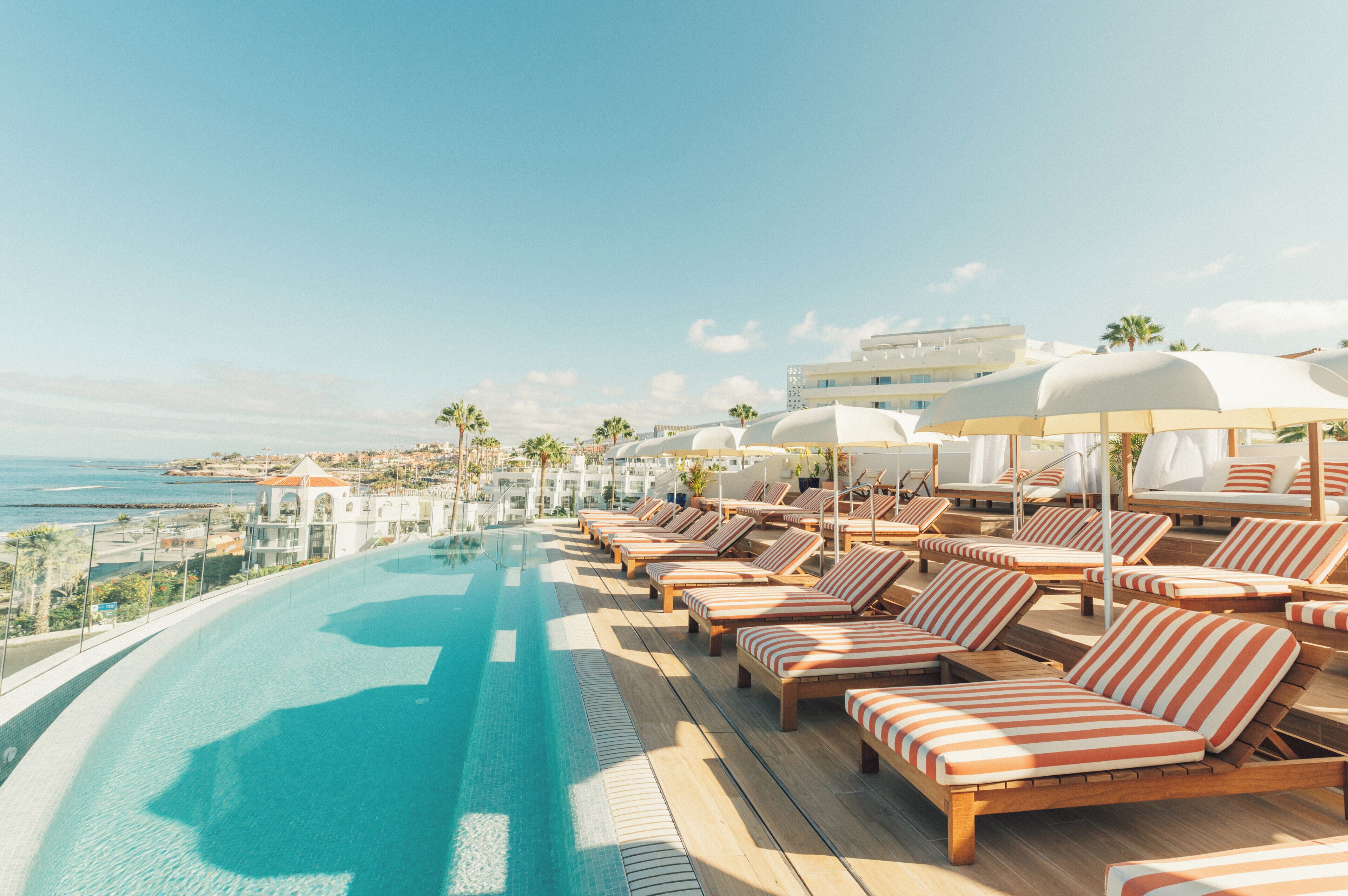 Ein Poolbereich mit Liegestühlen und Sonnenschirmen mit Blick auf die Küste.