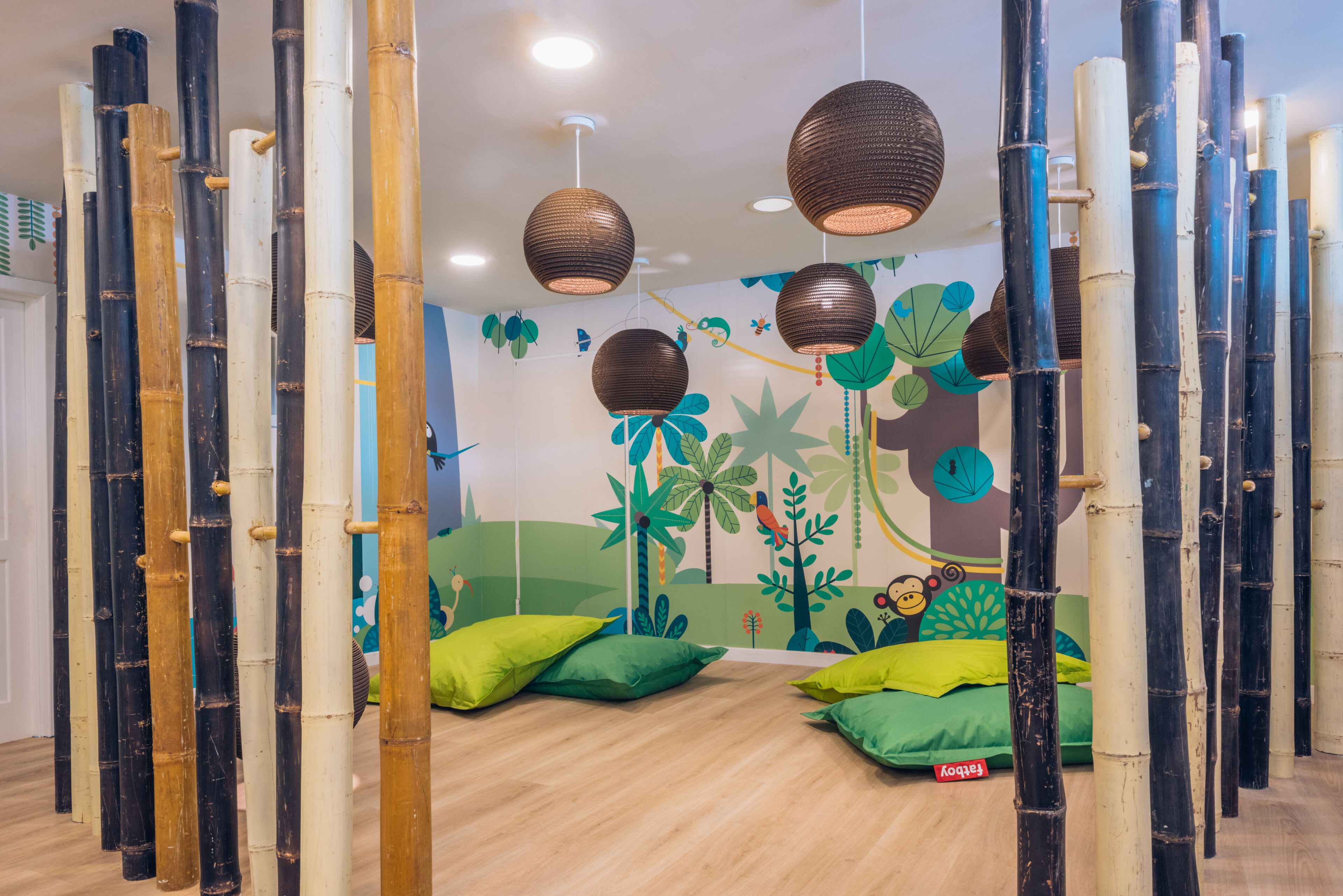 A room with bamboo pillars, green cushions, and a mural with a monkey and palm trees.