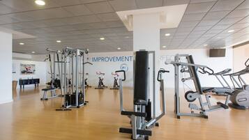 Un gimnasio con diversas máquinas de ejercicio, piso de madera y un cartel que dice 'IMPROVEMENT'.
