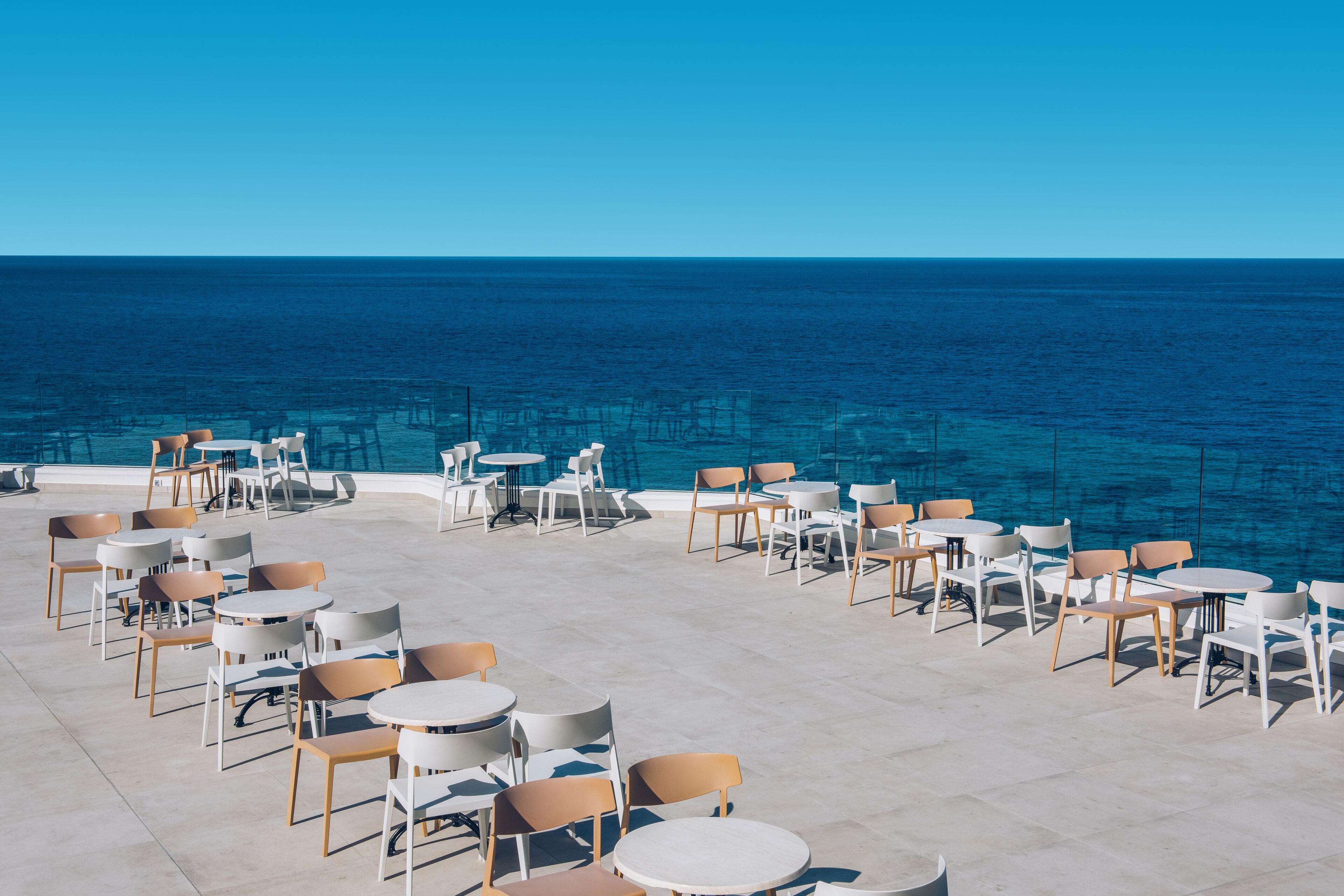 An outdoor seating area with tables and chairs facing a large body of water.