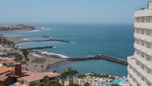 Un complejo turístico en la costa con playa, un rompeolas rocoso y una zona de piscina.