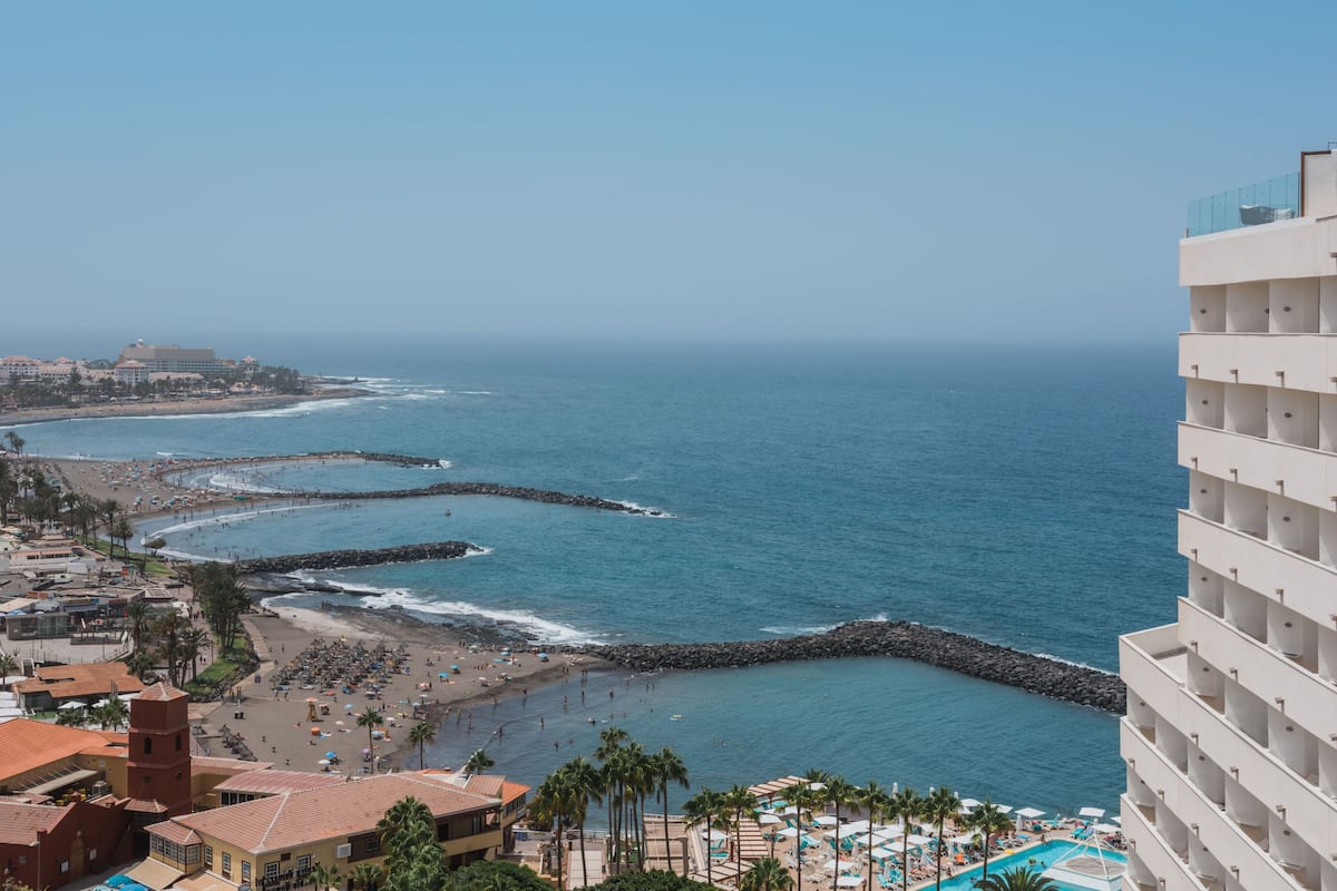 Um resort costeiro com praia, um molhe rochoso e área de piscina.