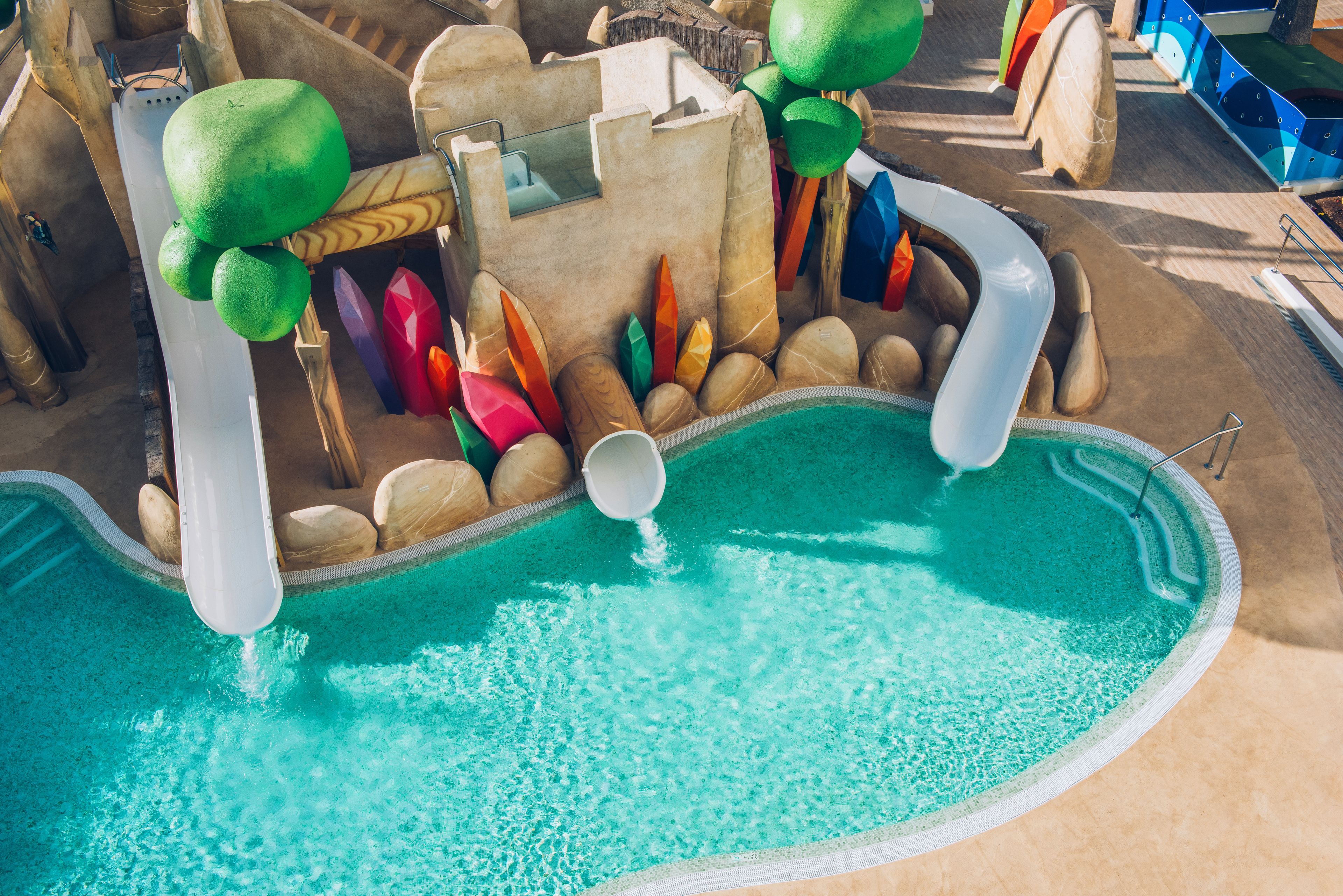 Un espace piscine doté d’un toboggan, de rochers aux couleurs vives et d’une structure en bois.