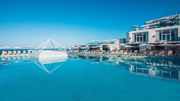 Un hotel moderno con una amplia piscina infinita, tumbonas y una vista despejada del océano.