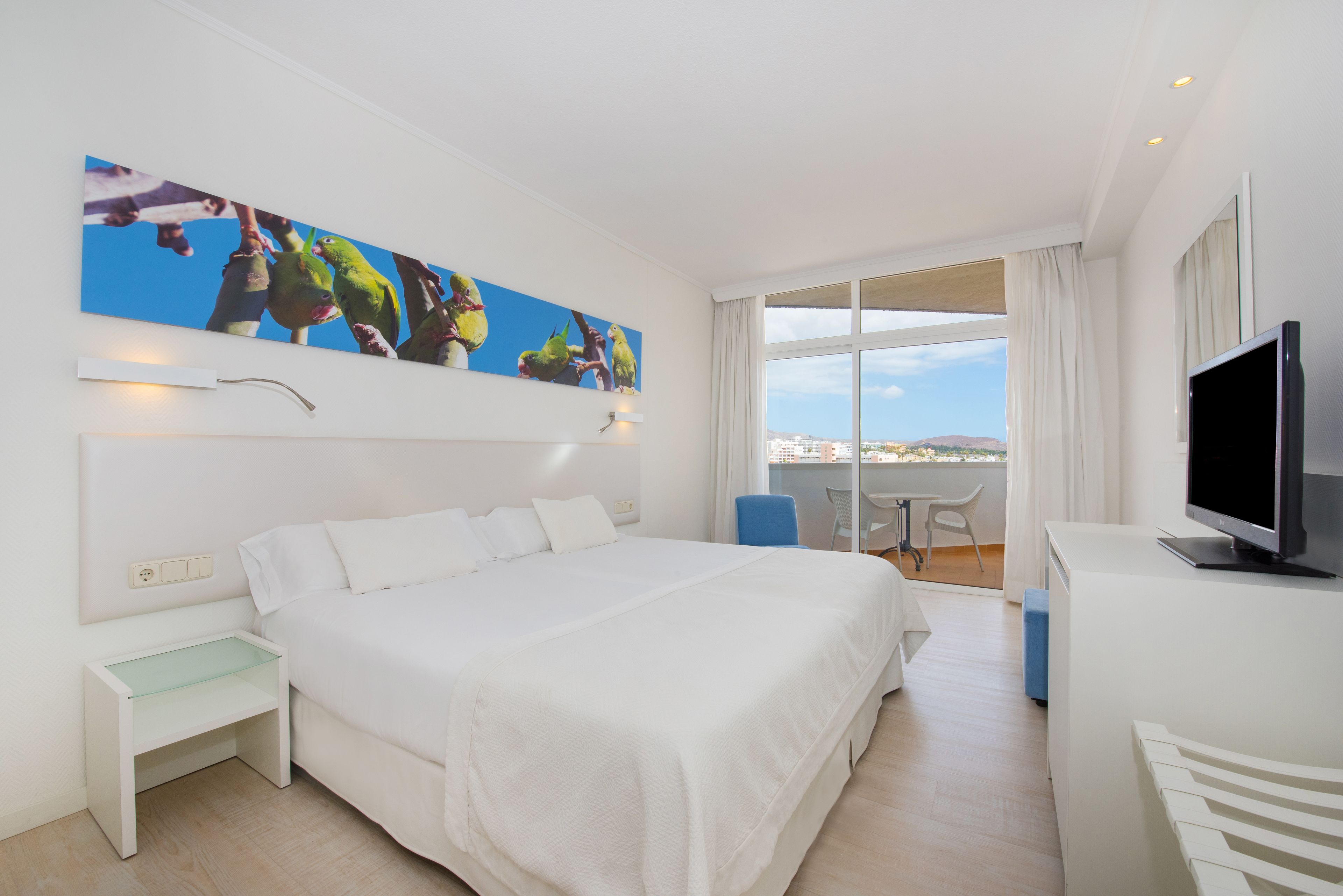 A hotel room with a large bed, a desk, a television, and a window with a view of the city.