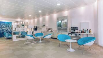 A modern hotel lobby with teal chairs, a white reception desk, and a kitchen area.