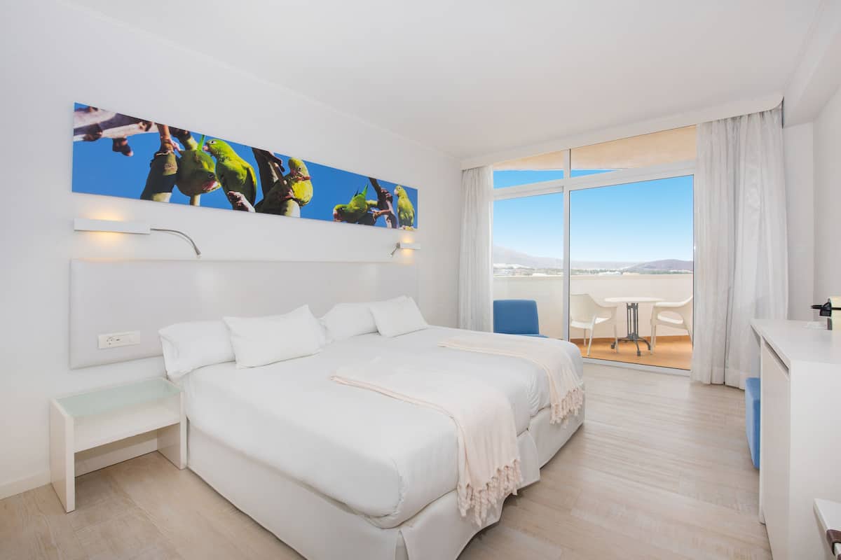 Quarto de hotel com cama grande, mesa de trabalho, cadeira e varanda com vista.