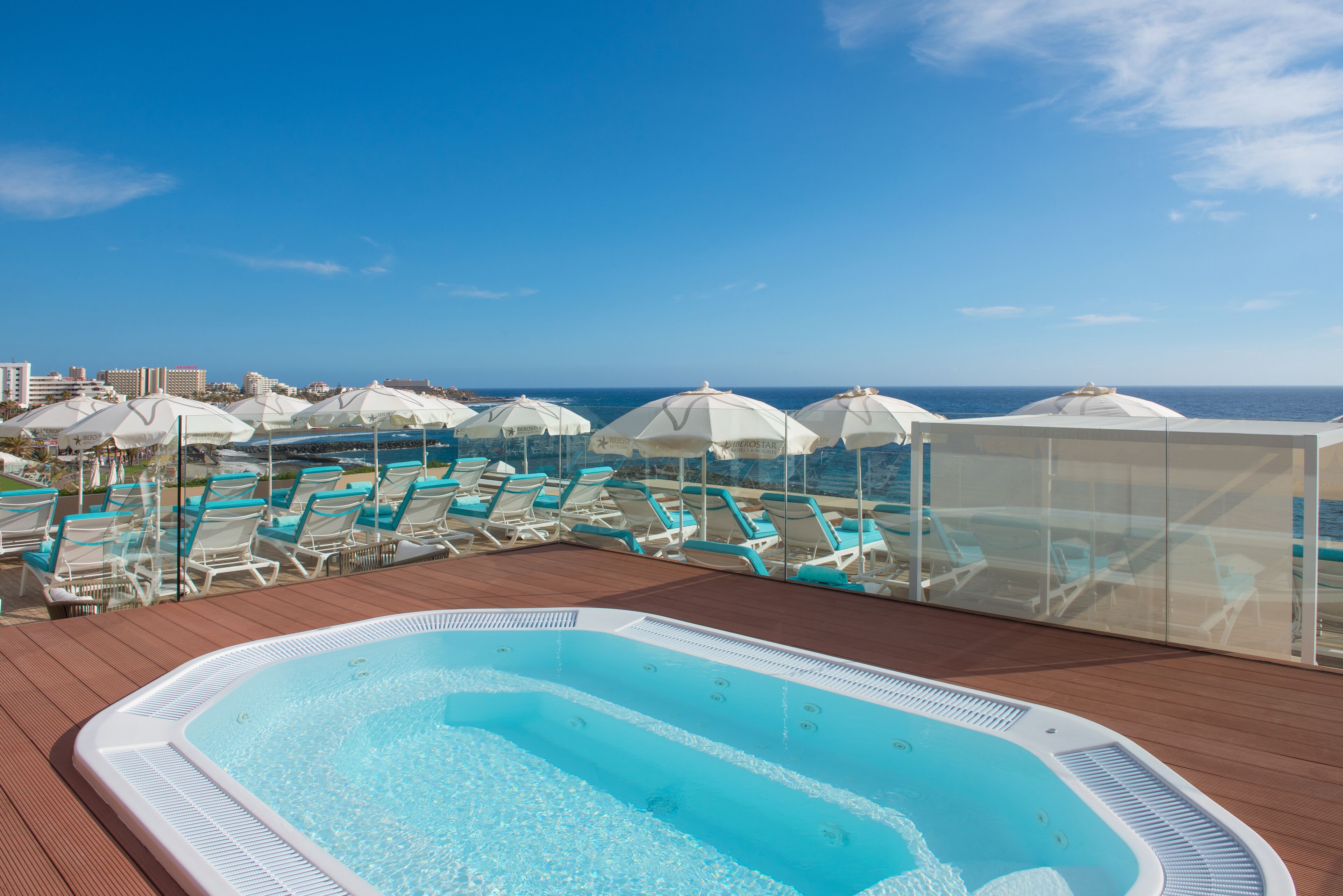 Un espace piscine aménagé sur le toit, avec des chaises longues et des parasols, offrant une vue sur l’océan.