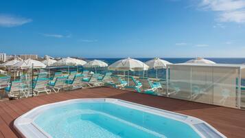 Un espace piscine aménagé sur le toit, avec des chaises longues et des parasols, offrant une vue sur l’océan.