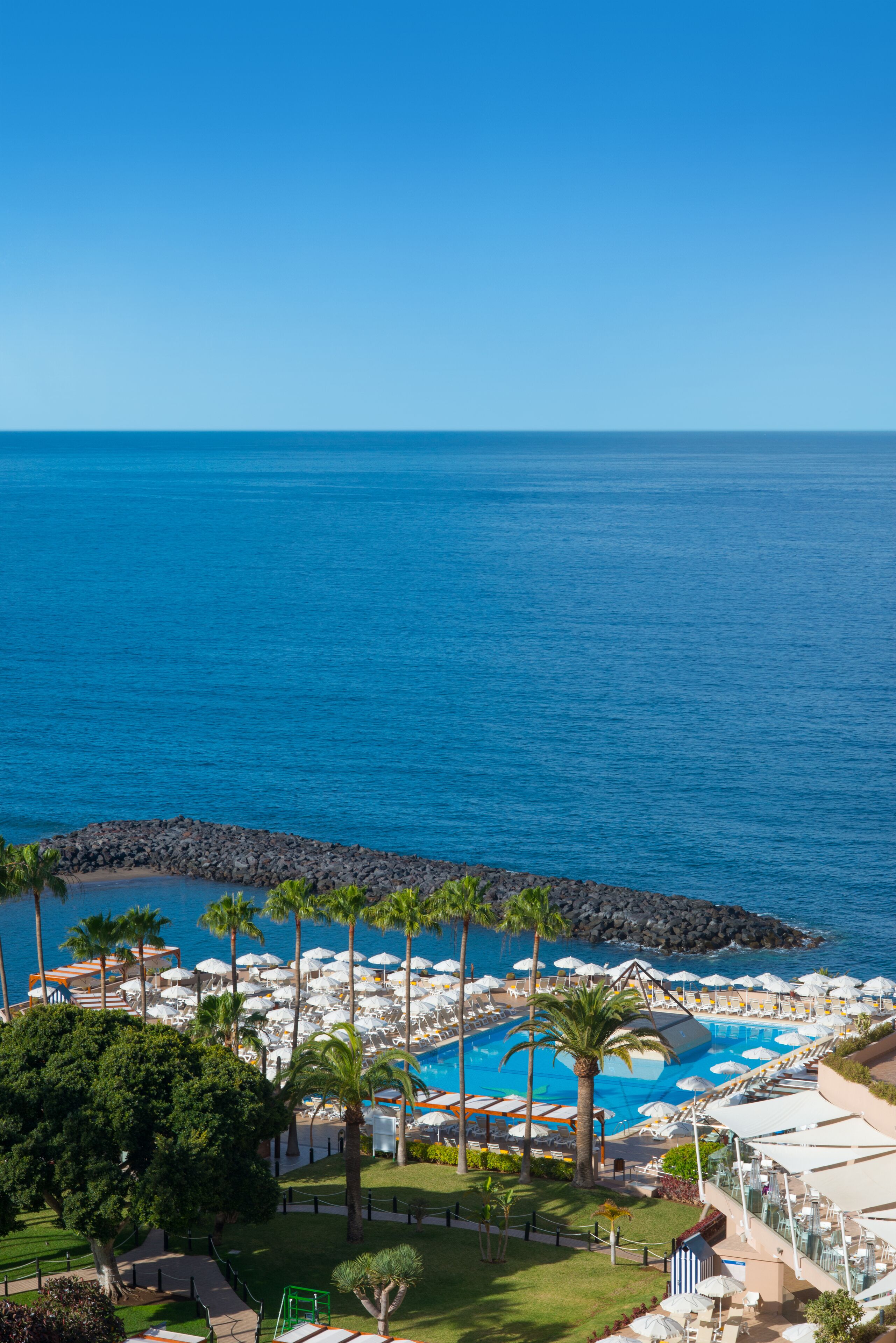 A resort with a pool area, palm trees, and a view of the ocean.
