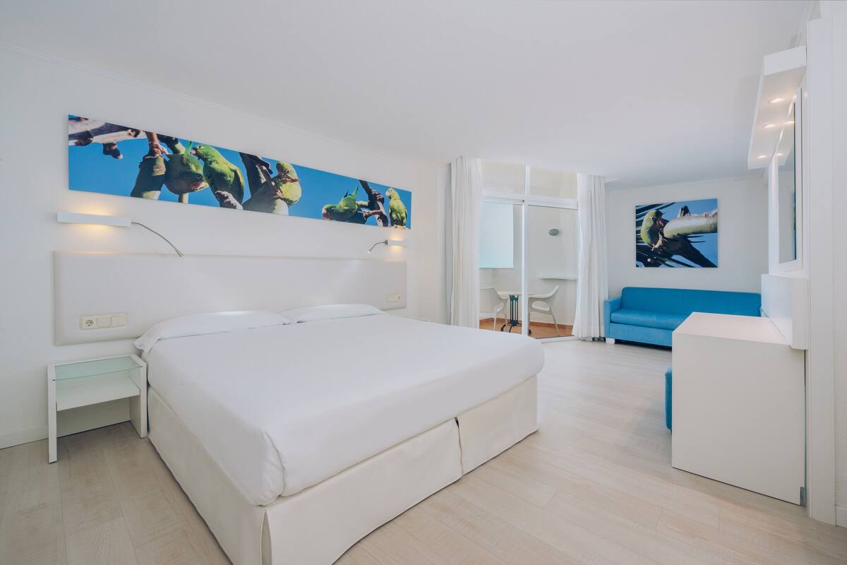 Quarto moderno com uma cama grande, um sofá azul e obras de arte nas paredes.