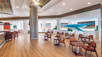 A spacious indoor area with wooden flooring, multiple tables and chairs, a central pillar, and large windows with a mural view.