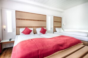 Une chambre d’hôtel avec deux lits, une tête de lit en bois, un plaid rouge et une table de chevet avec une lampe.