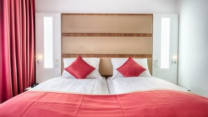 Una habitación de hotel con una cama grande, cortinas rojas y un cabecero de madera.