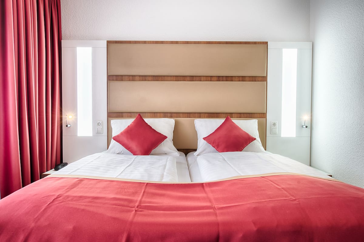 A hotel room with a large bed, red curtains, and a wooden headboard.