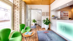 Un vestíbulo de hotel con sillas verdes, un mostrador de recepción y vistas a la calle a través de un escaparate.
