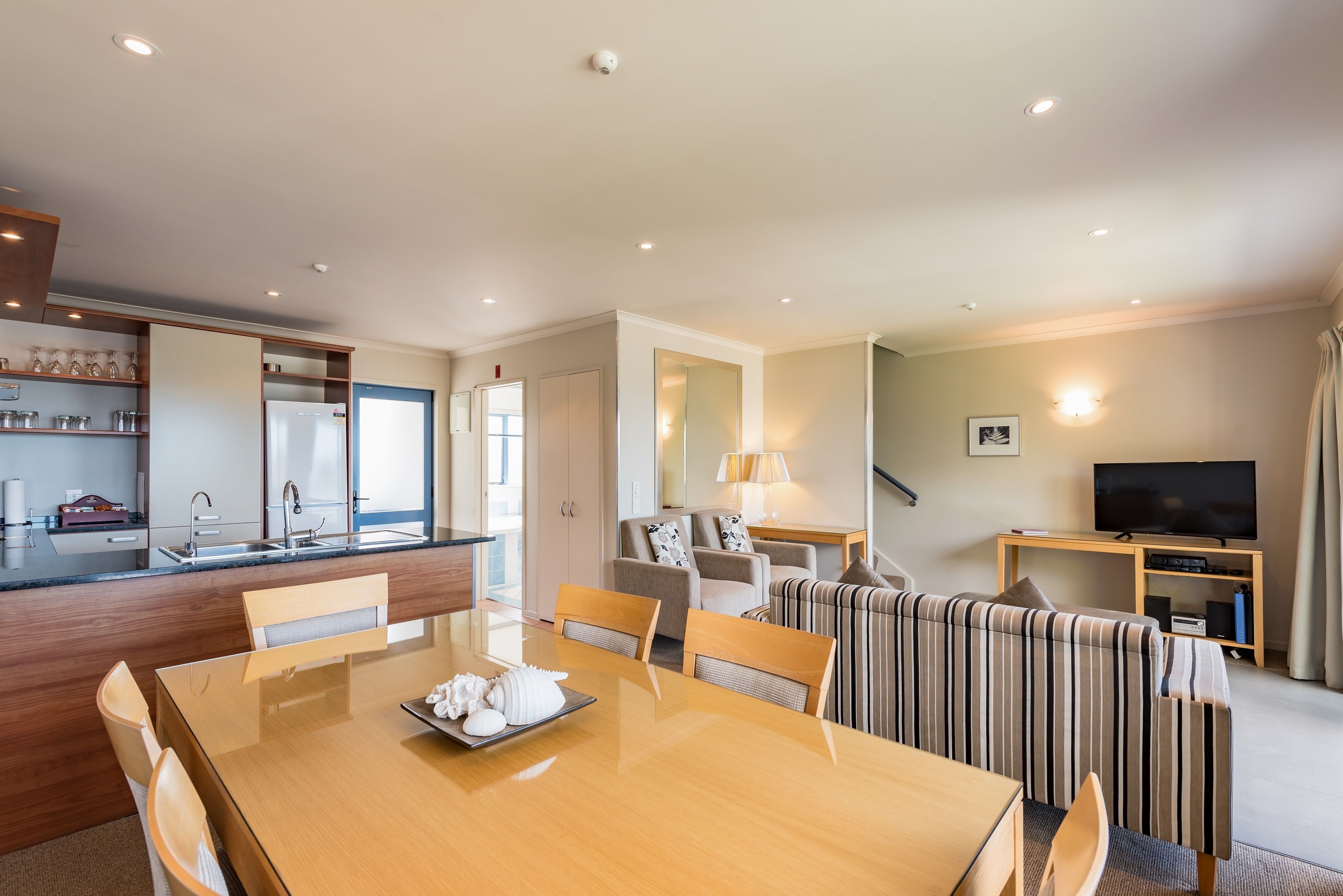 Ein modernes Wohnzimmer mit Essplatz, Sofas, einem Fernseher und einer Küchenzeile inklusive Kühlschrank und Schränken.