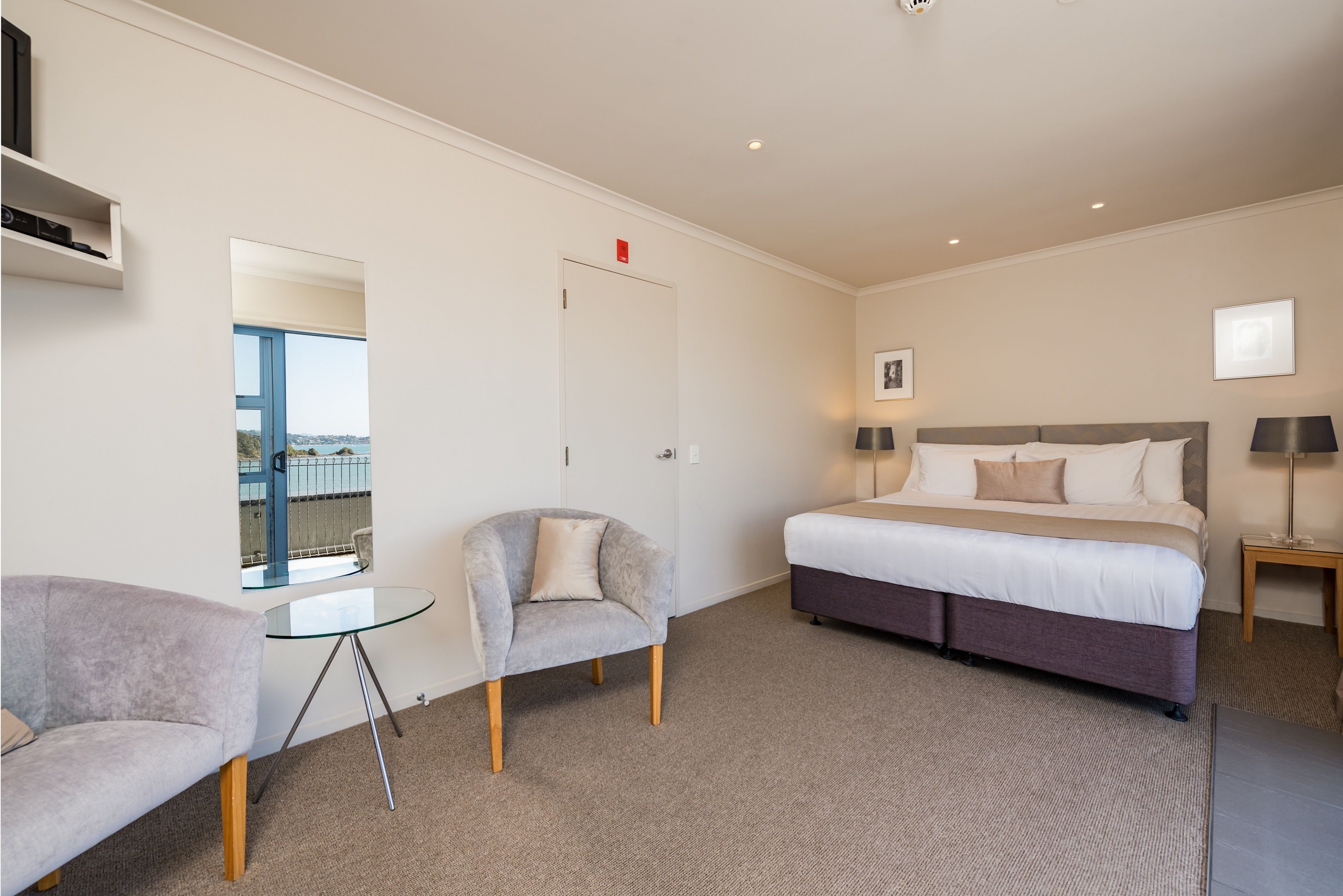 Ein Hotelzimmer mit Bett, Sessel, kleinem Tisch, Nachttisch und Fenster mit Blick.