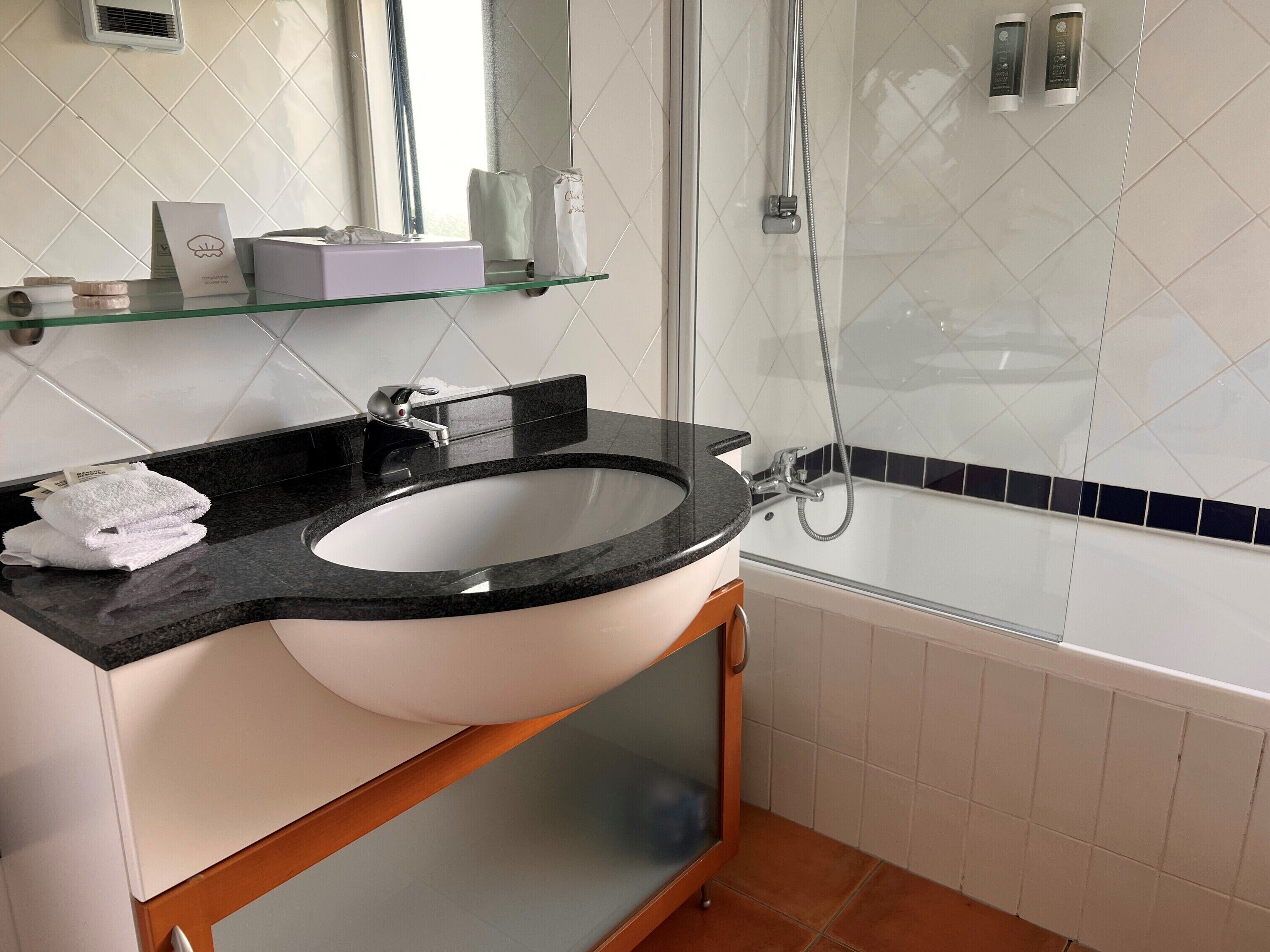 Een badkamer met een zwarte granieten wastafel, een glazen douchecabine en een betegelde muur in het wit.