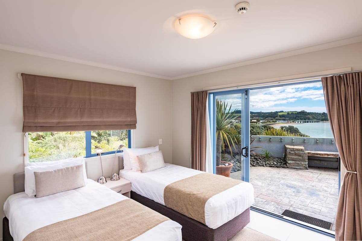Ett hotellrum med två sängar, ett stort fönster med utsikt över havet och en balkong med en mur av sten.